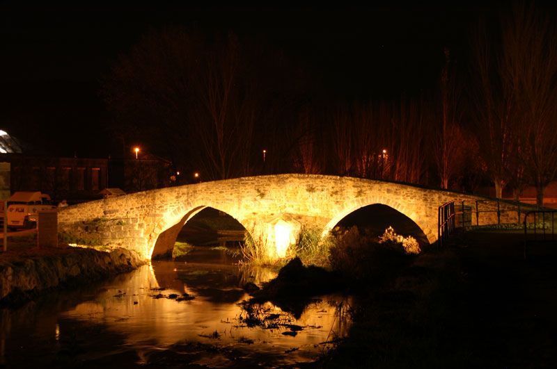 Un puente de piedra se ilumina por la noche sobre un río.