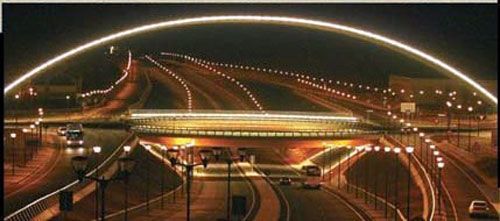 Una carretera está iluminada por la noche con un puente al fondo.