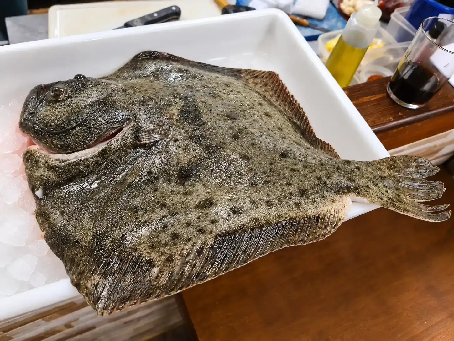 Un pescado plano entero en una bandeja en un mostrador de preparación de alimentos.