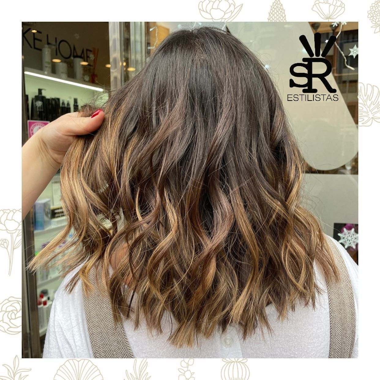 Cabello castaño ondulado con reflejos de una mujer. Una mano lo sujeta, posiblemente en una peluquería.