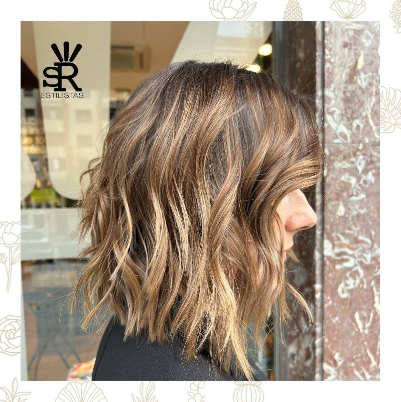 Mujer con cabello castaño ondulado, reflejos bronceados, en un salón de belleza.