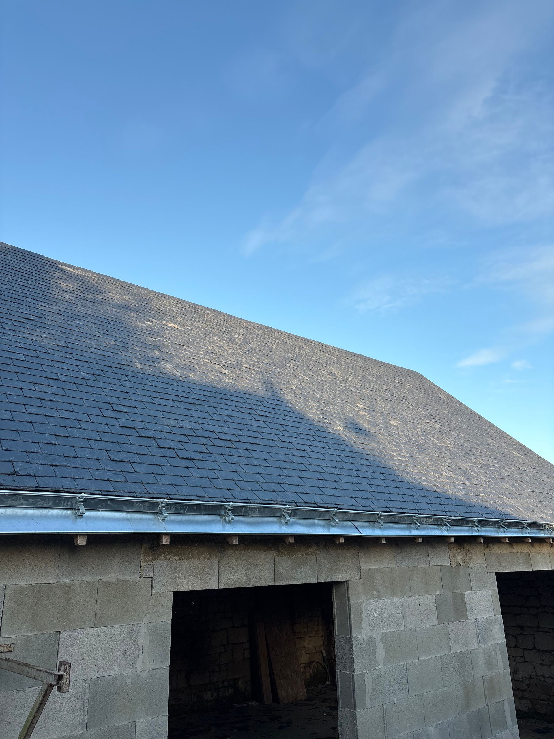 Toit en bardeaux gris sur un bâtiment en pierre, se détachant sur un ciel bleu.