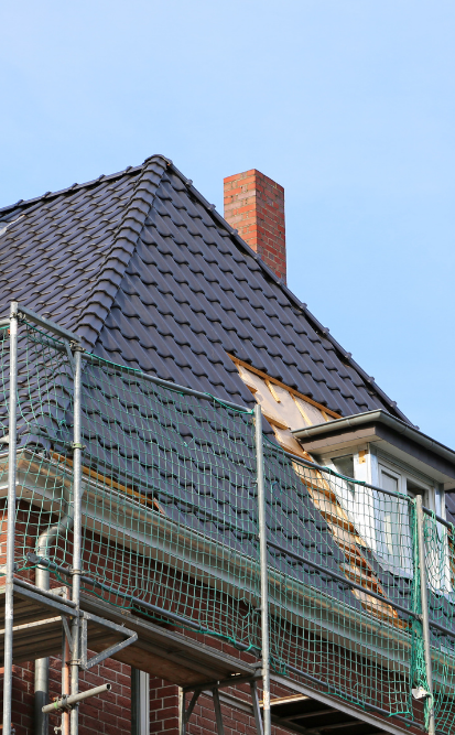 Toiture d'un bâtiment en cours de réparation, avec échafaudages et tuiles gris foncé partiellement remplacées.