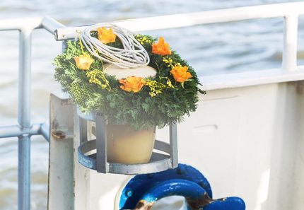 Urne am Wasser Urne mit Blumenkranz an der Reling für eine Seebestattung.