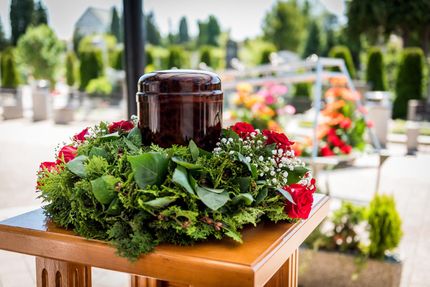 Urne mit Kranz Braune Schmuckurne mit grünem Blumenkranz im Freien.