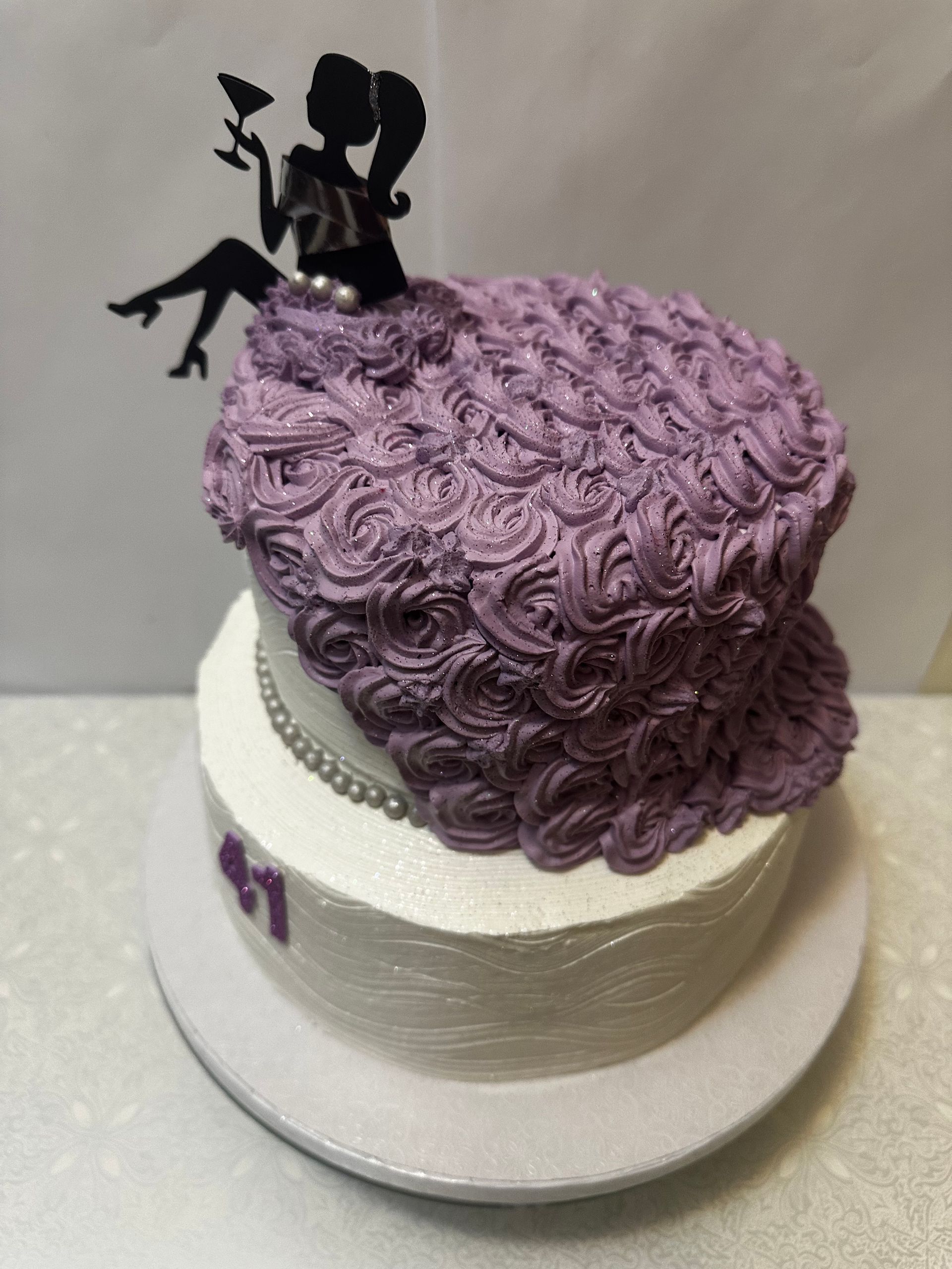 Un pastel blanco con glaseado morado y una silueta de una mujer en la parte superior.