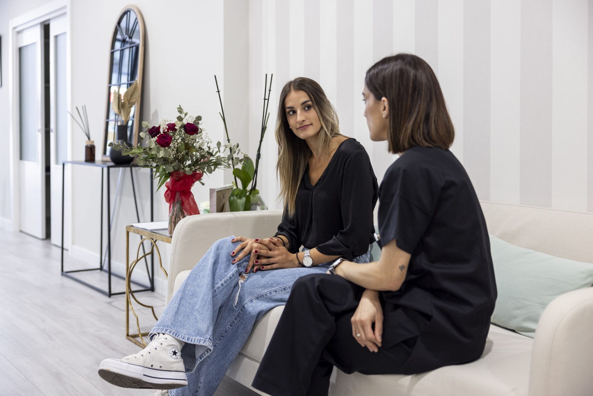 Dos mujeres están sentadas en un sofá hablando entre sí.