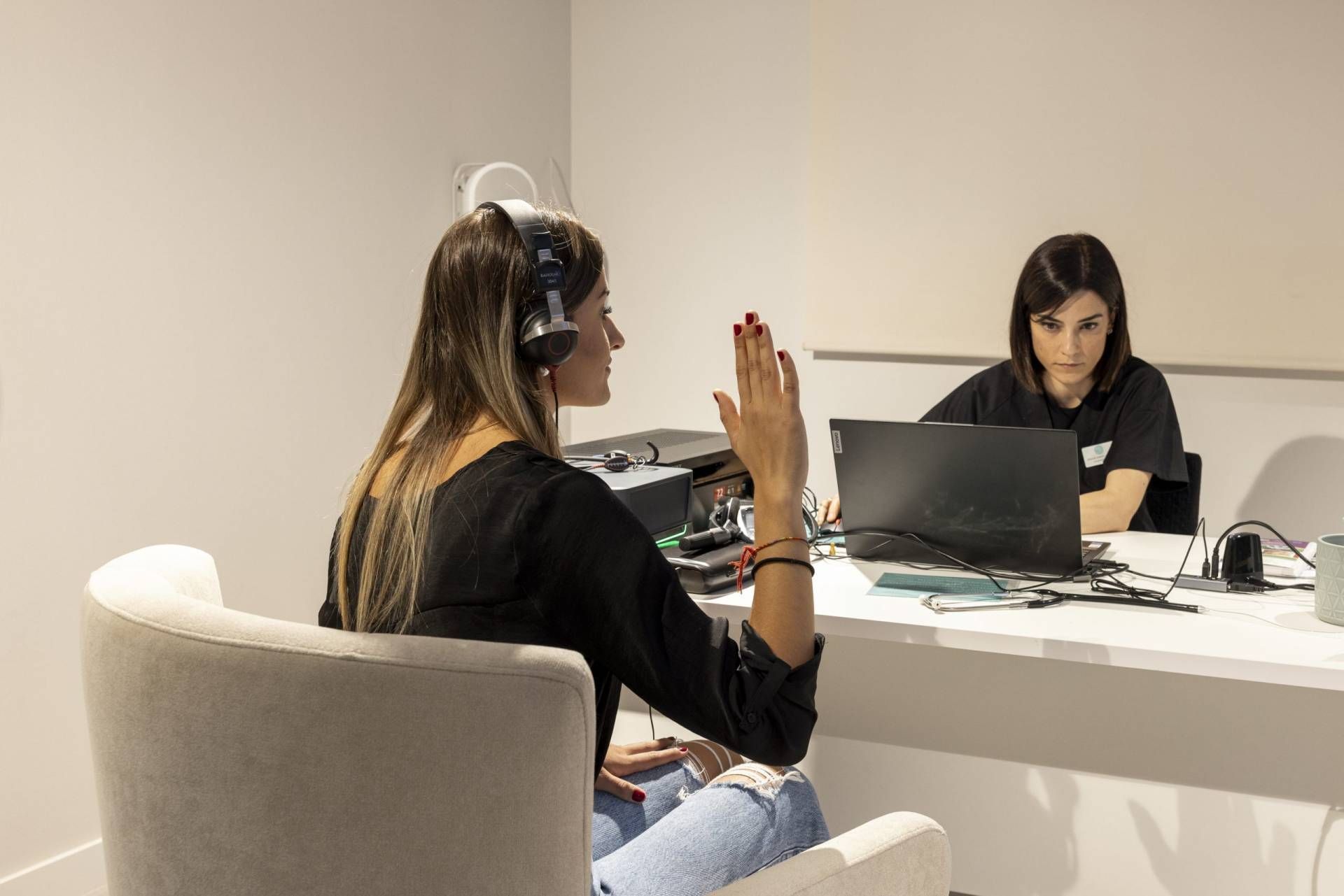 Una mujer con auriculares está sentada en un escritorio hablando con otra mujer.