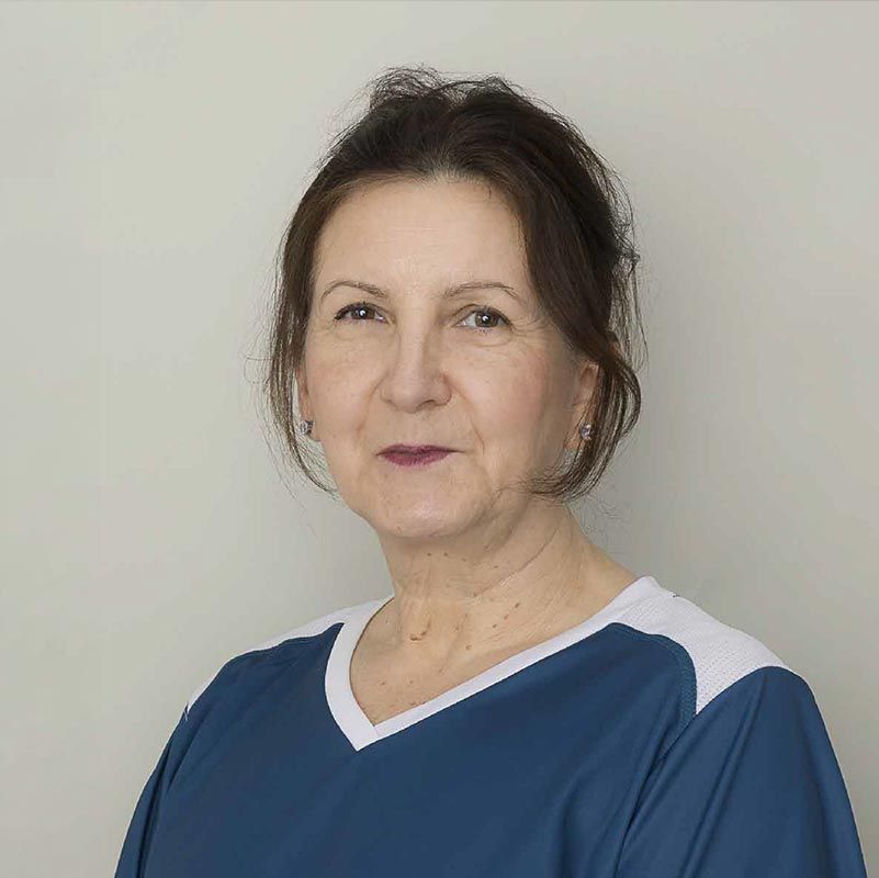 Eine Frau in einem dunkelblauen Hemd steht vor einem hellen Hintergrund und blickt mit einem leichten Lächeln in die Kamera.