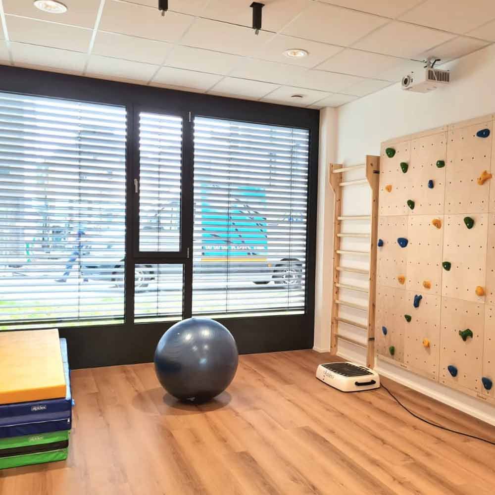 Leerer Fitnessraum mit Gymnastikball, Kletterwand, Balancematten und großen Fenstern