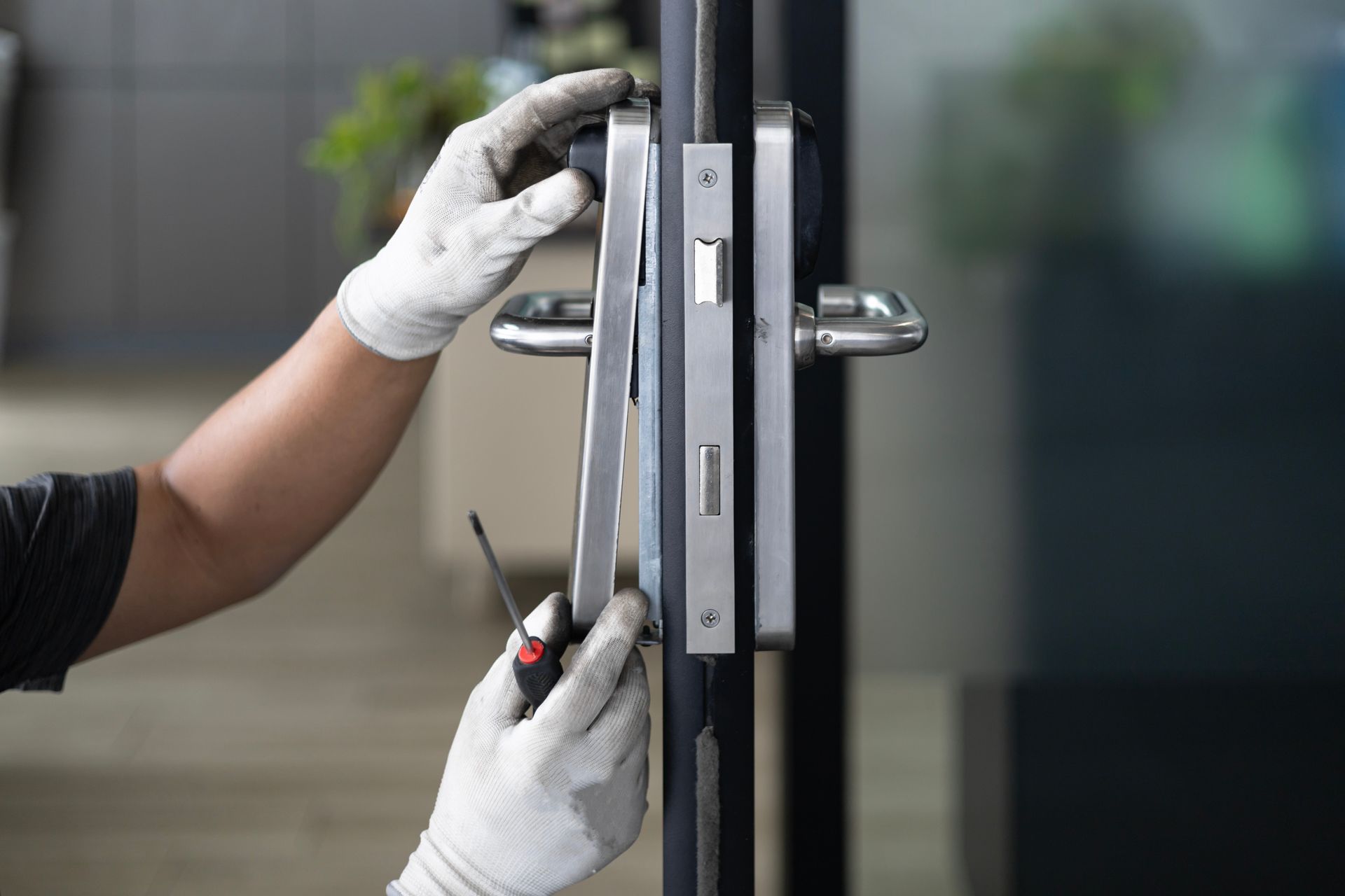 Des mains gantées utilisent des outils pour installer une serrure sur une porte de bureau vitrée.