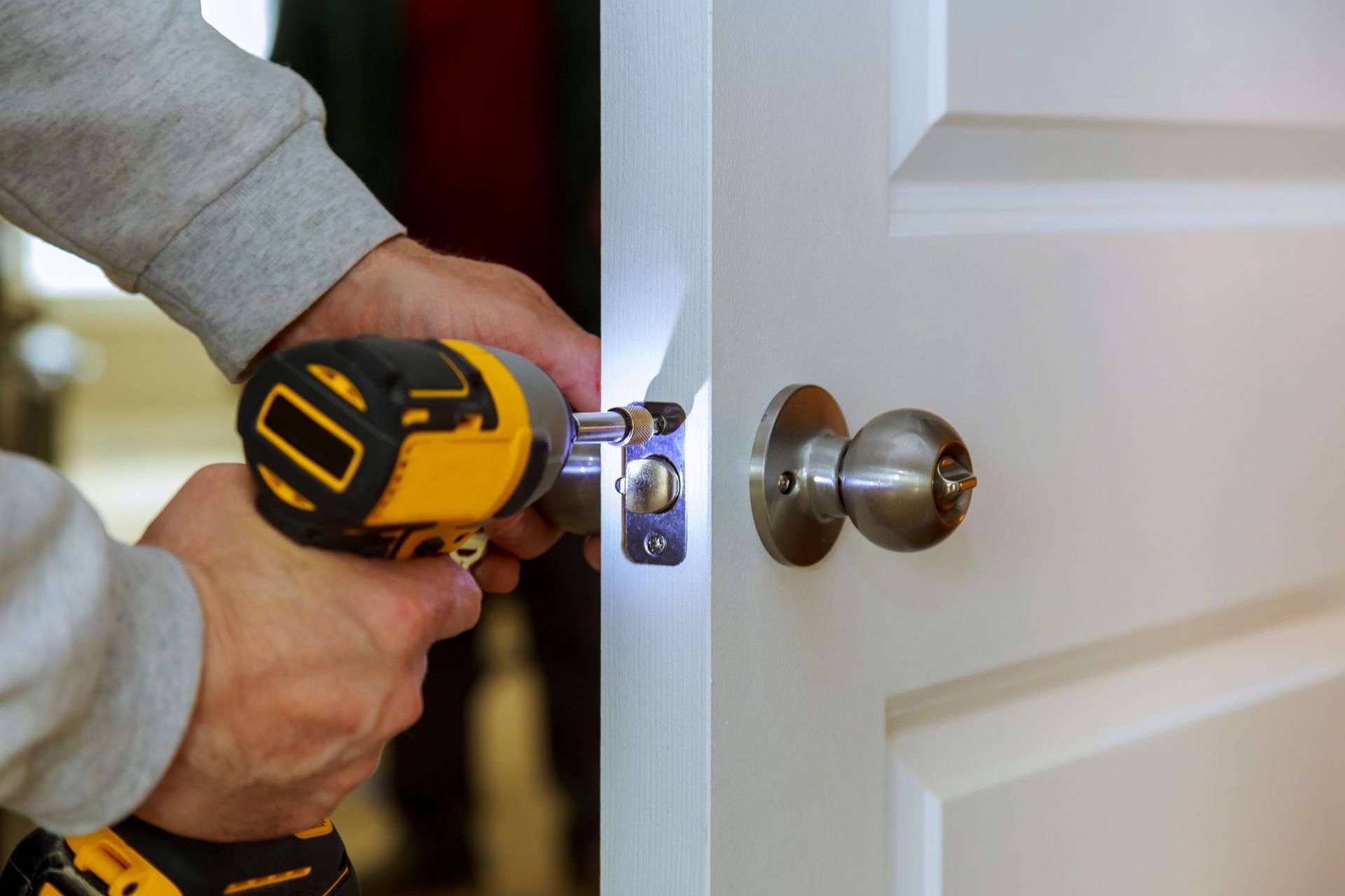 Personne utilisant une perceuse jaune pour installer une serrure argentée sur une porte blanche