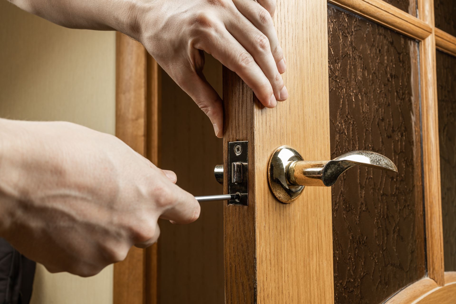 Des mains installent une serrure sur une porte vitrée en bois avec une poignée chromée.