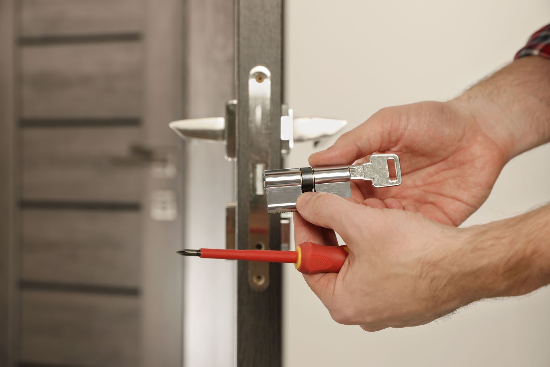 Un homme change la serrure d'une porte d'entrée à l'aide d'un tournevis rouge.