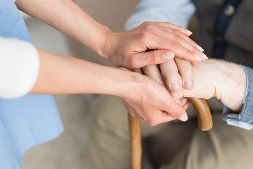 Mains jointe entre soigante et homme âgé avec une canne