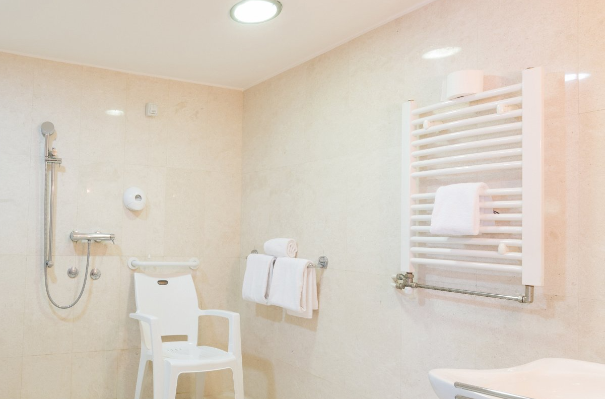 Salle de douche aménagée avec chaise de douche, barre d'appui dans la douche