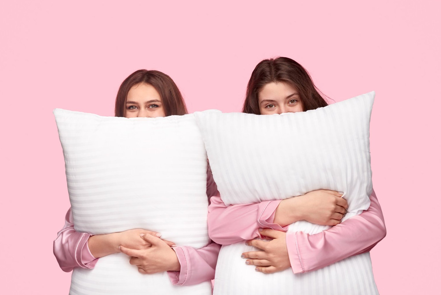 Deux jeunes femmes avec deux oreillers, fond rose uni