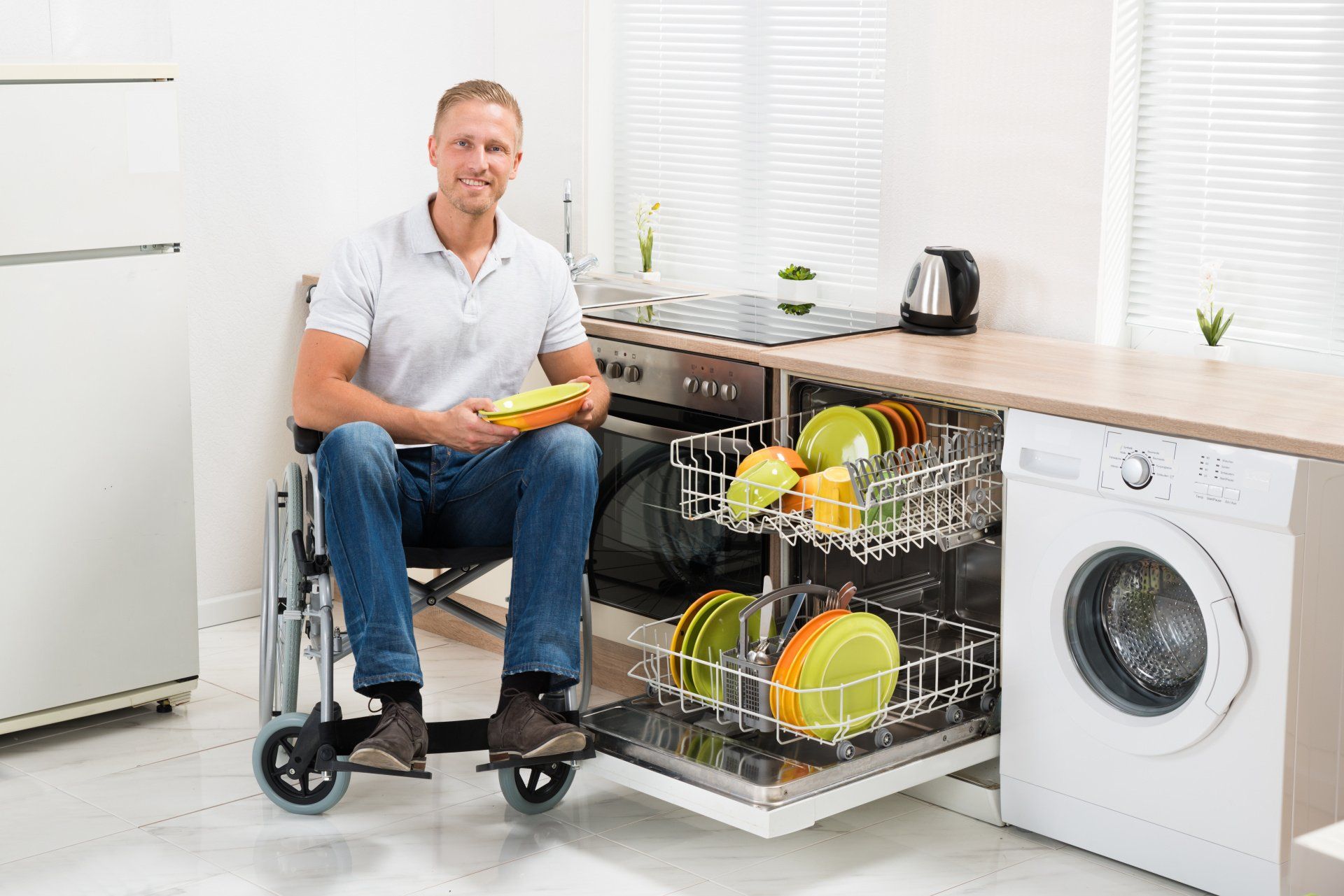 Homme en fauteuil roulant devant lave-vaisselle rempli avec de la vaisselle adaptée