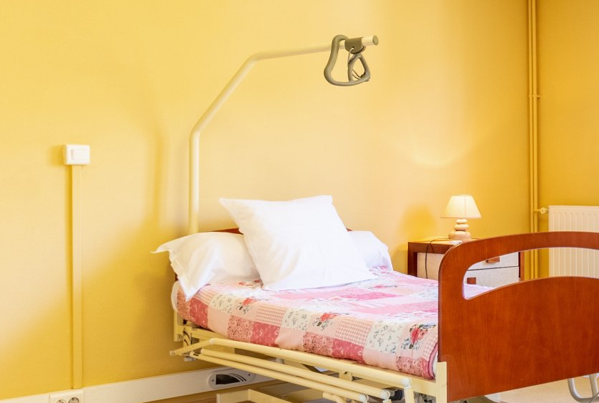 Mur jaune chambre avec lit médicalisé et potence