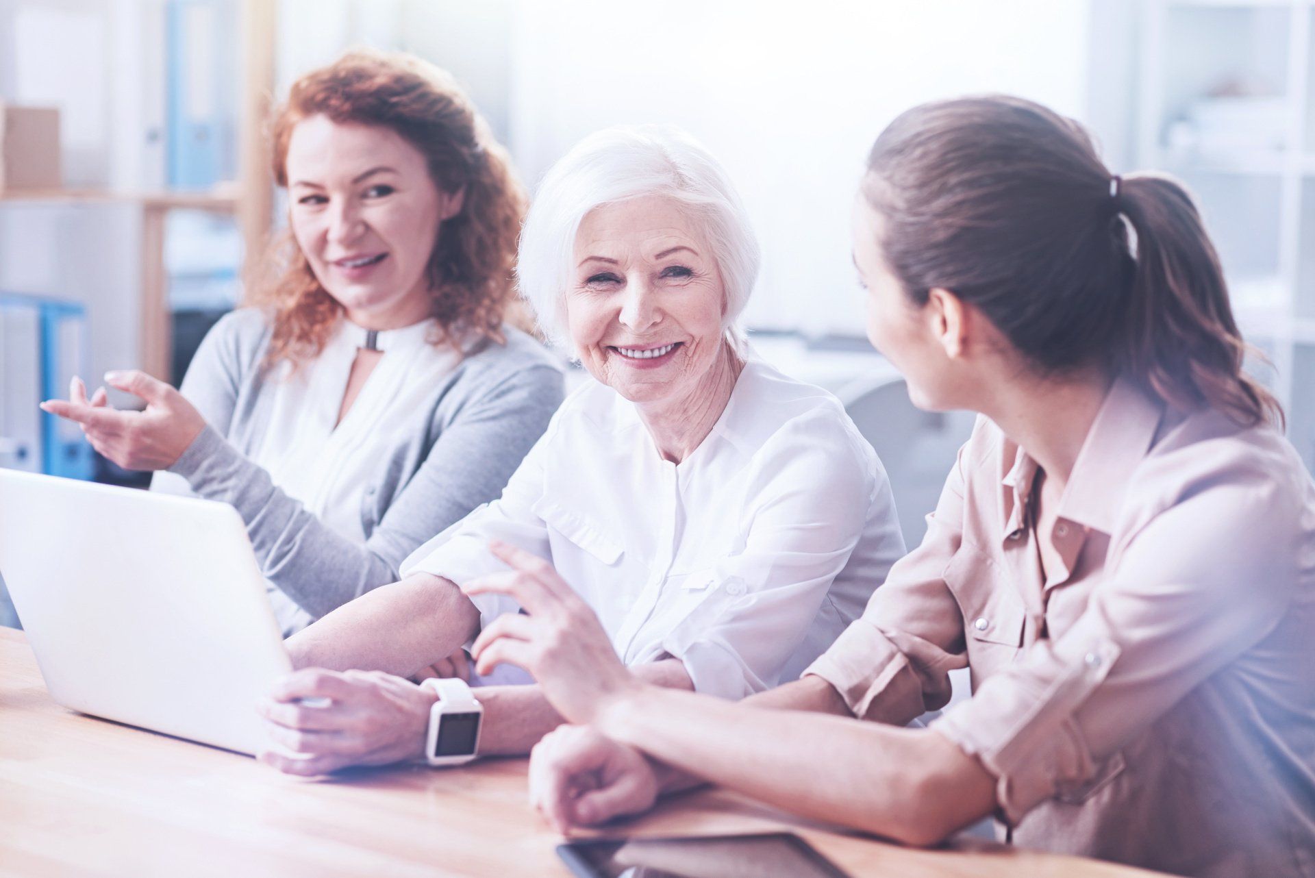 Femmes parlant souriantes, dont une senior avec un ordinateur
