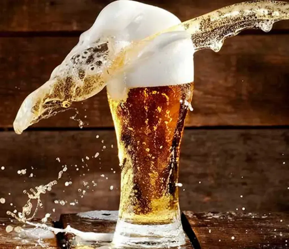 Un vaso de cerveza con espuma saliendo de él sobre una mesa de madera.