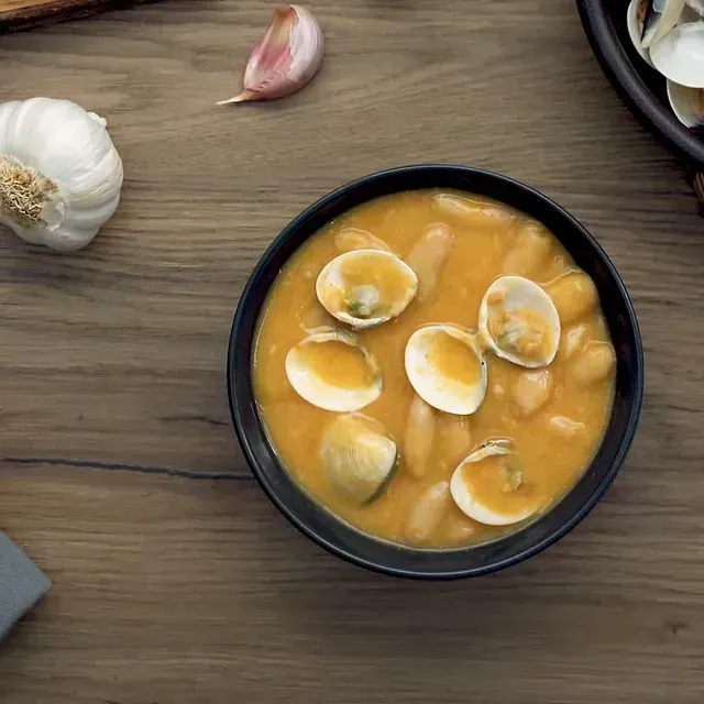 Un tazón de sopa con almejas y frijoles en una mesa de madera.