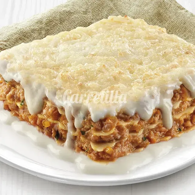 Un trozo de lasaña en un plato blanco con una servilleta.