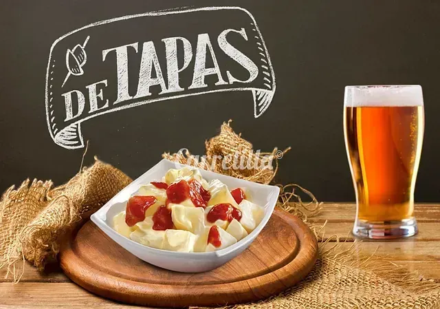 Un plato de comida junto a un vaso de cerveza y un cartel que dice de tapas