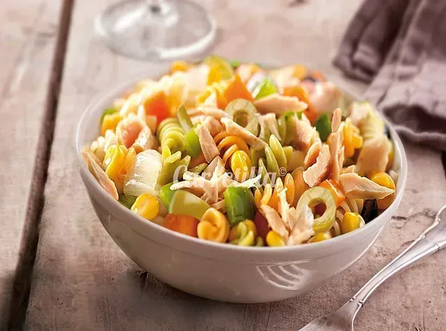 Un tazón de ensalada de pasta con atún y verduras sobre una mesa de madera.