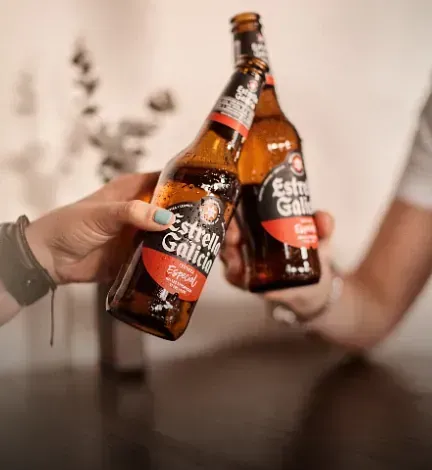 Dos personas sostienen botellas de cerveza Estrella Galicia.