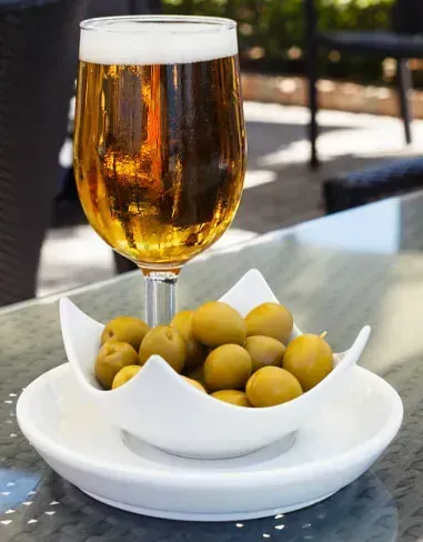 Un vaso de cerveza y un bol de aceitunas en una mesa