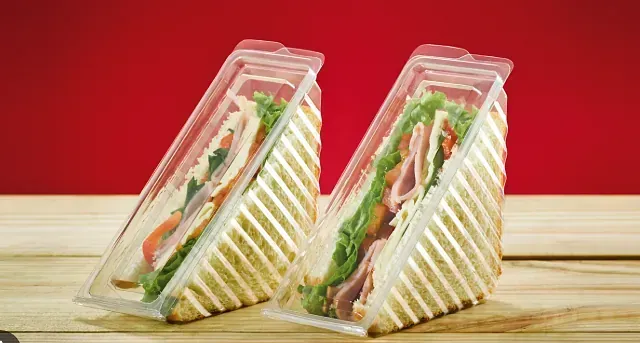 Dos sándwiches en recipientes de plástico sobre una mesa de madera.