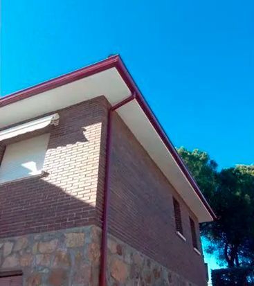 Una casa de ladrillo con un canalón rojo y un cielo azul al fondo.