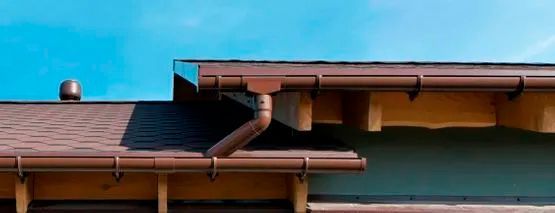 Una casa con una canaleta marrón y un cielo azul al fondo.