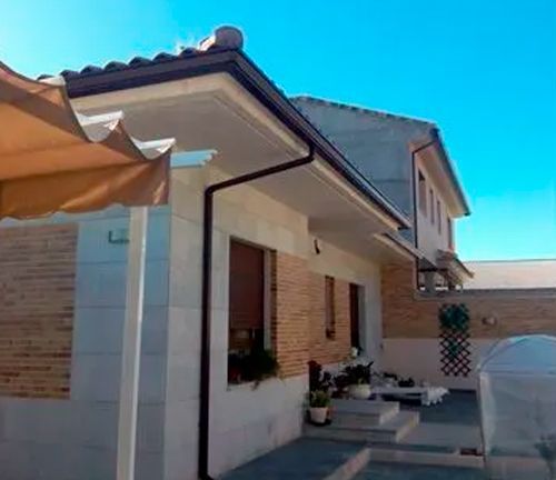 Una casa con una canaleta al costado y una sombrilla en el porche.