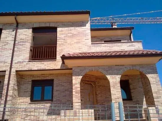 Se está construyendo una gran casa de ladrillo con arcos y balcón.