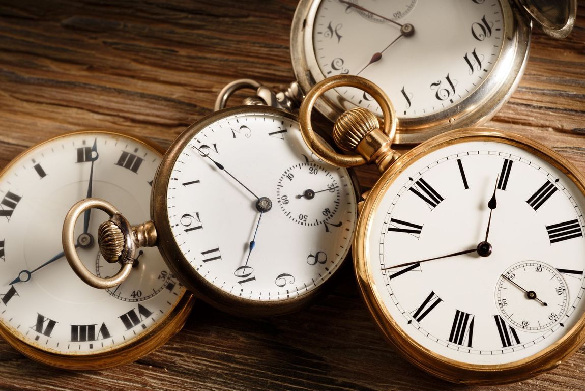 Quatre montres de poche anciennes à cadran blanc et boîtier en or, posées sur un support en bois.