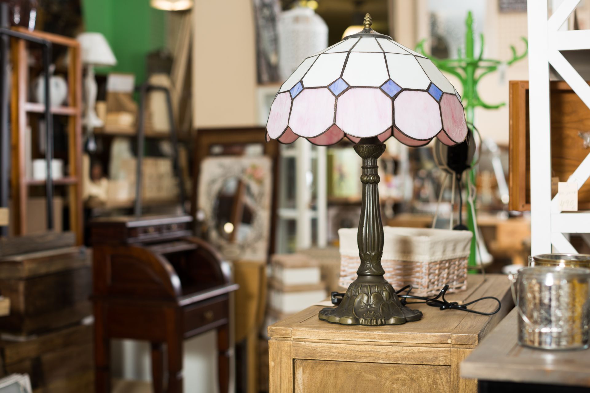 Une lampe en vitrail ornée de détails roses et bleus est posée sur une armoire en bois dans un magasin de meubles.