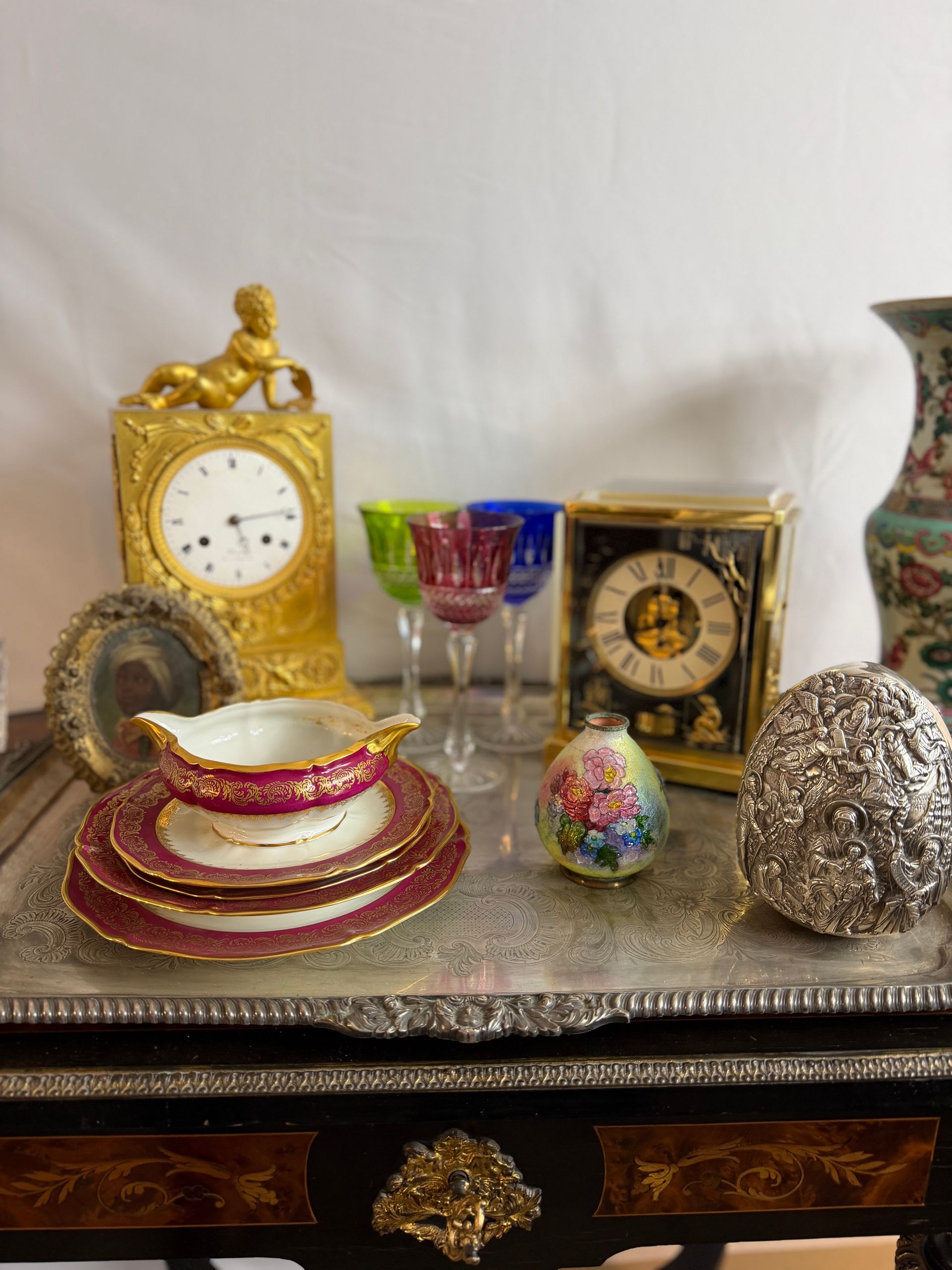 Plateau en argent avec horloges anciennes, verres colorés et objets décoratifs.