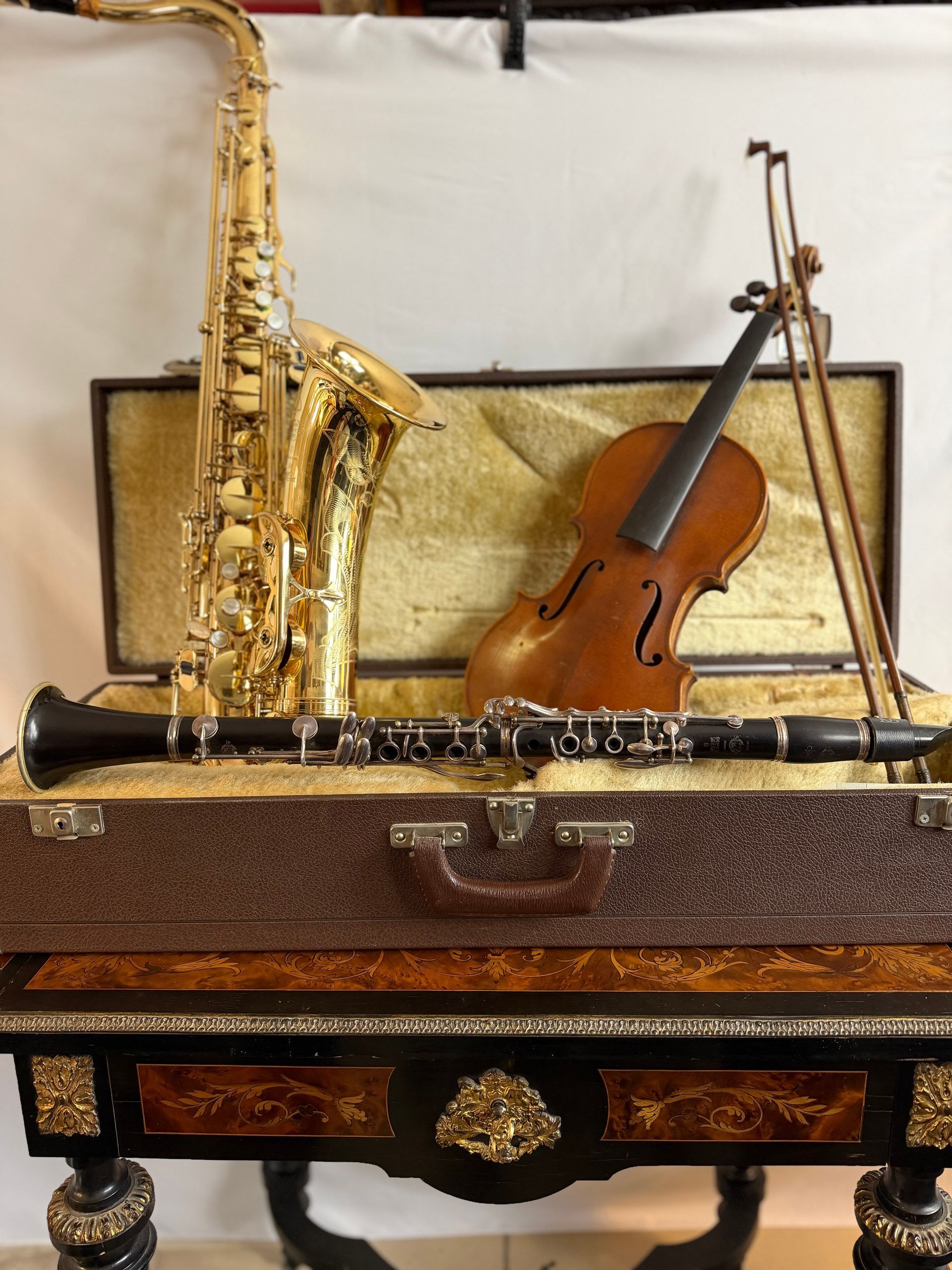 Saxophone, violon et clarinette sur une table décorative avec des étuis à instruments ; or, marron et noir.