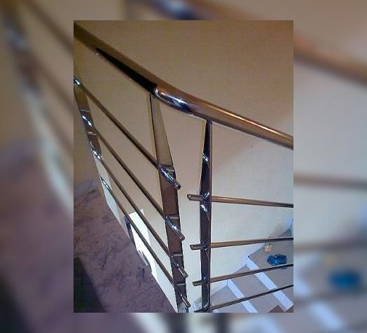 Primer plano, tomado desde un ángulo elevado, de una barandilla de escalera de acero inoxidable pulido con finas barras horizontales.