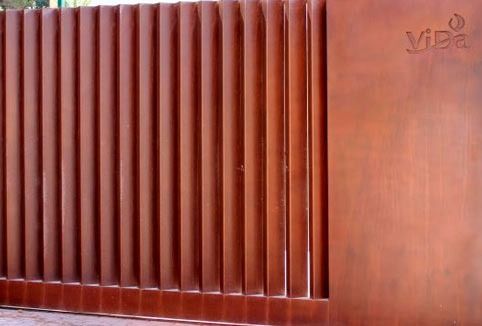 Una puerta de color óxido con listones verticales, fijada a una pared de metal macizo a juego con un pequeño logotipo