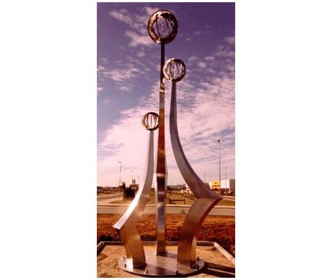 Una escultura alta de metal presenta tres soportes verticales curvos de diferentes alturas, cada uno rematado por una jaula esférica abierta.