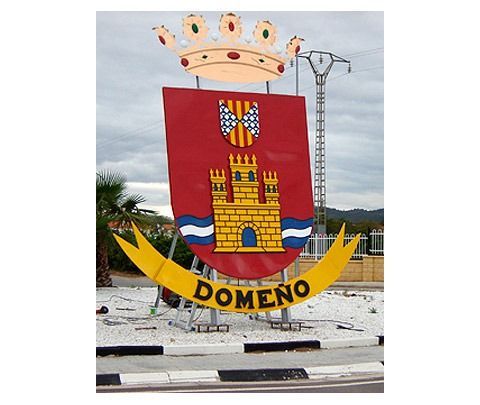 Un gran letrero de metal con el escudo de armas de Domeño, que incluye una corona dorada, un castillo y una pancarta amarilla con la inscripción 