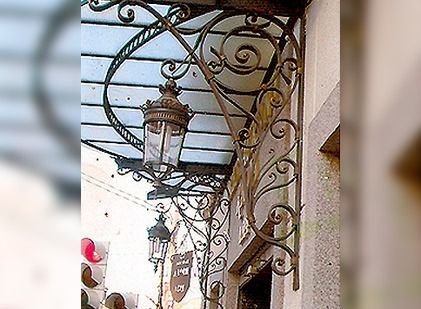 Toldo ornamentado de hierro forjado con una linterna de cristal colgante sobre una entrada.