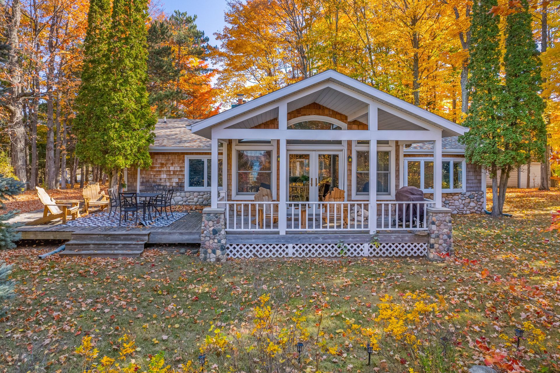 Cottage with porch surrounded by autumn foliage; yellow and orange leaves, sunny day.