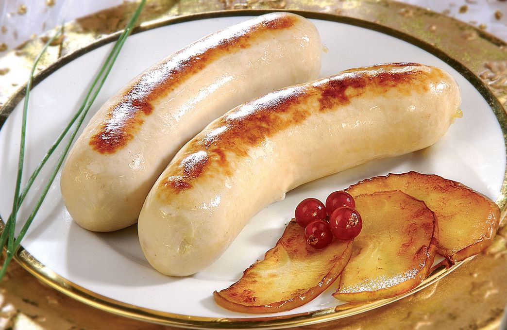 Saucisses grillées accompagnées de tranches de pomme et de canneberges, sur une assiette blanche à bord doré.