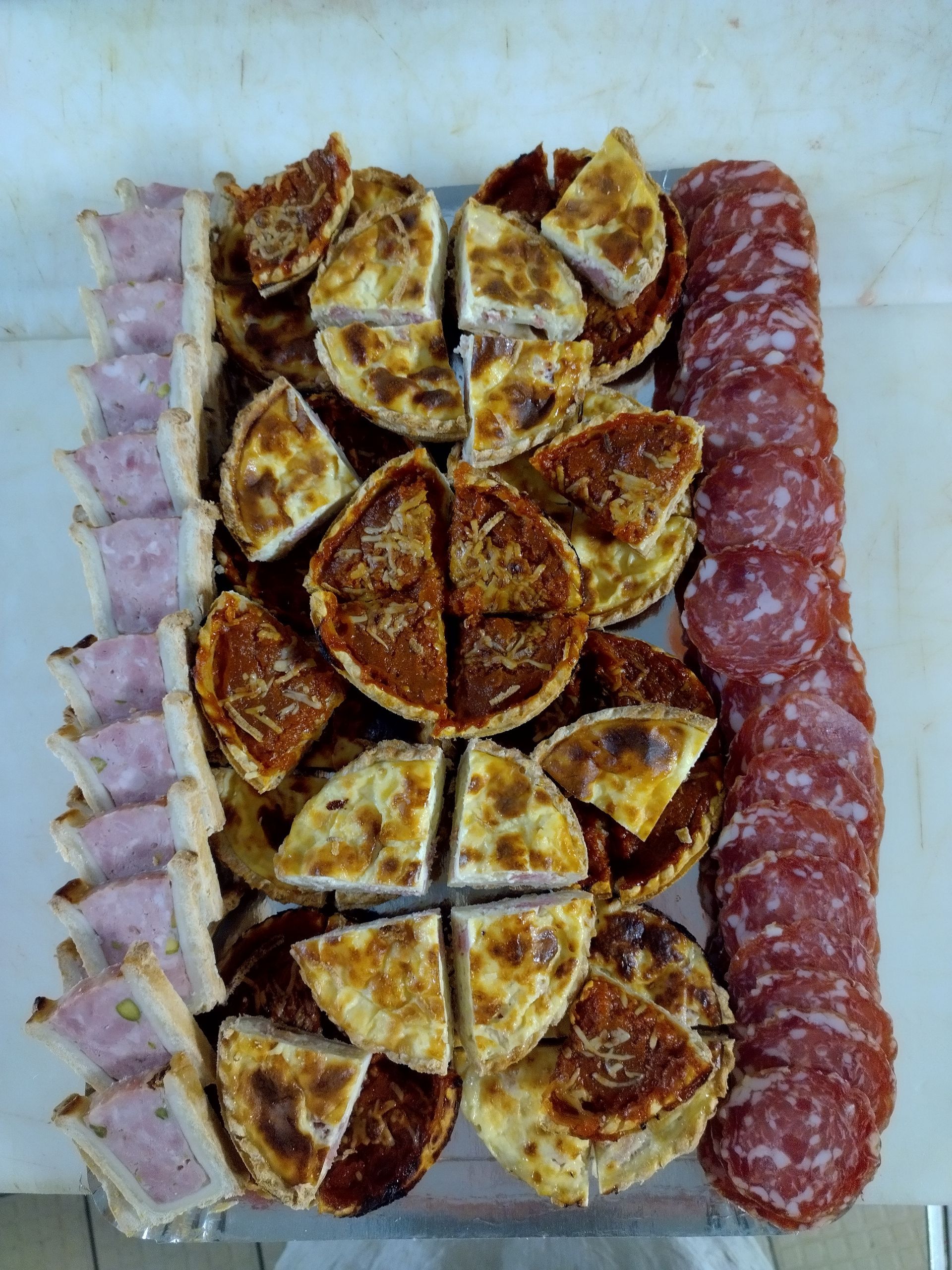 Assortiment charcuteries tranchés disposés sur un plateau, avec des quartiers de quiches et de pâtés en croûte.