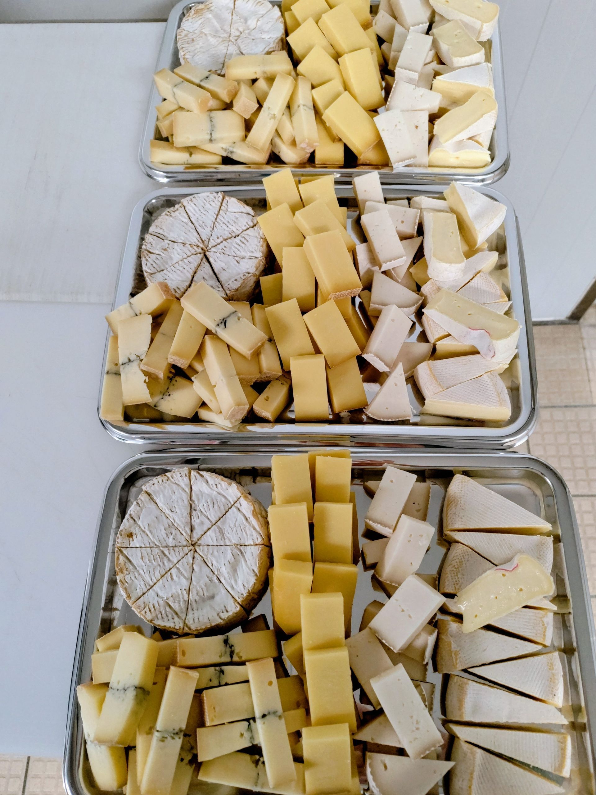 Trois plateaux de fromages assortis, coupés en pointes et en dés, sur une surface claire.