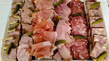 Assortiment de charcuterie avec des viandes tranchées, du salami, du jambon et des gressins disposés en rangées.